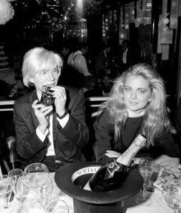 Andy Warhol sharing a bottle of Moët Impérial at a dinner in New York City with socialite Cornelia Guest, 1985. ©Ron Galella